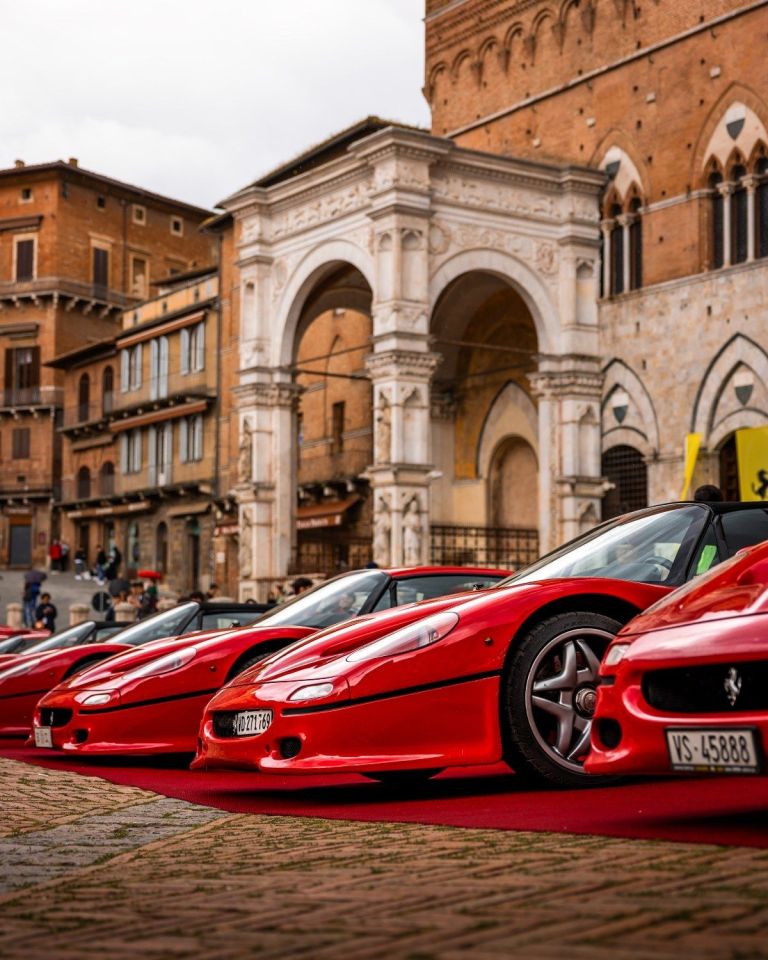 Row of red Ferrari cars parked in historic Italian plaza.