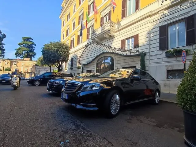 Luxury cars parked outside a historic building with a scooter nearby.